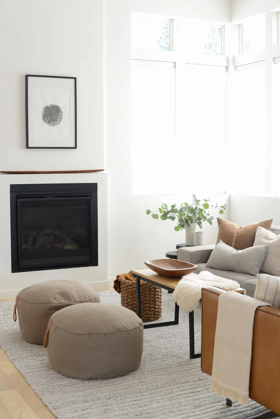 A living room styled by Design Club, with a fireplace, linen poufs and a wood bowl on the coffee table